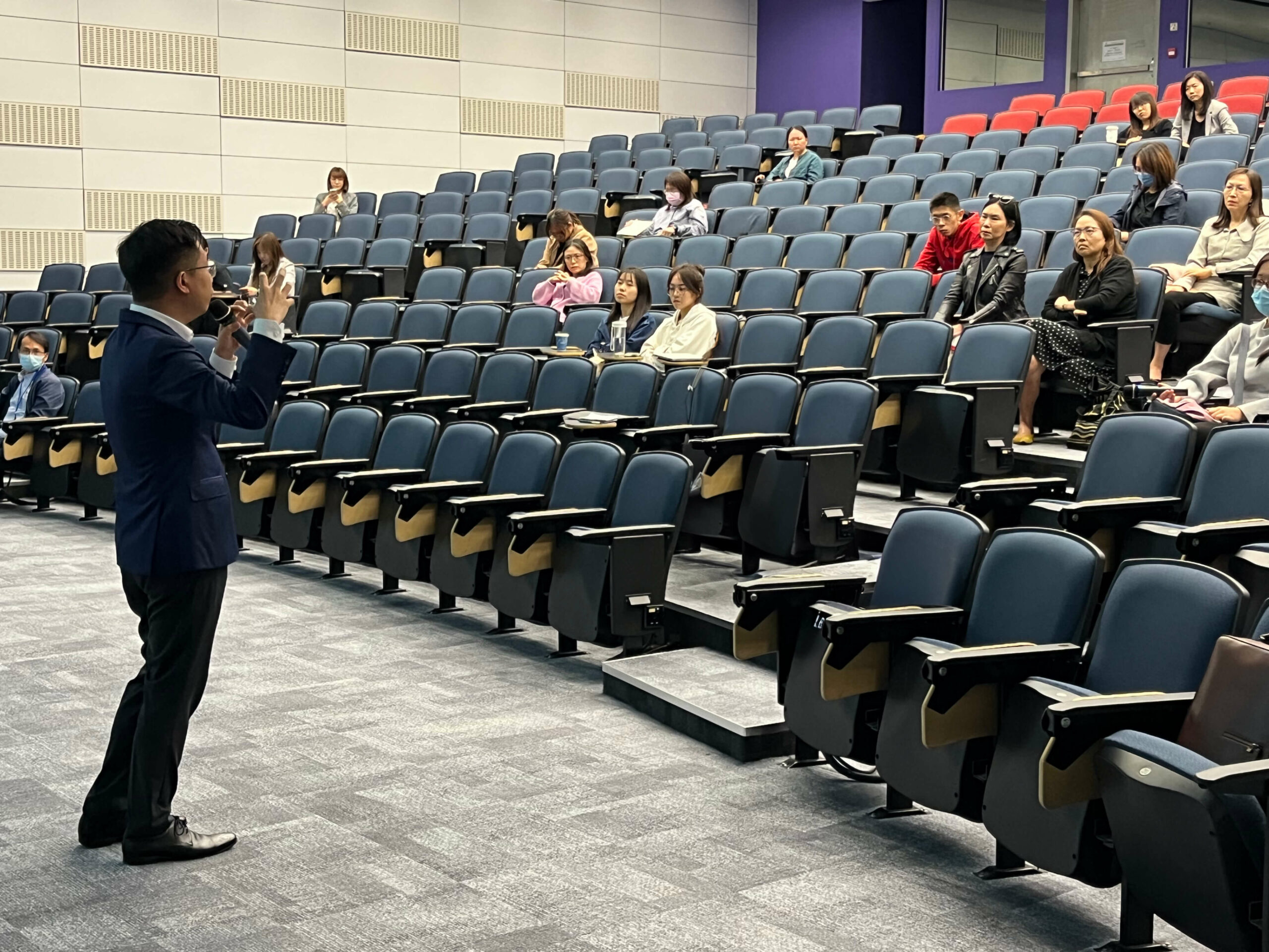 A close-up of the guest speaker talking to the audience, gesturing with his right hand.