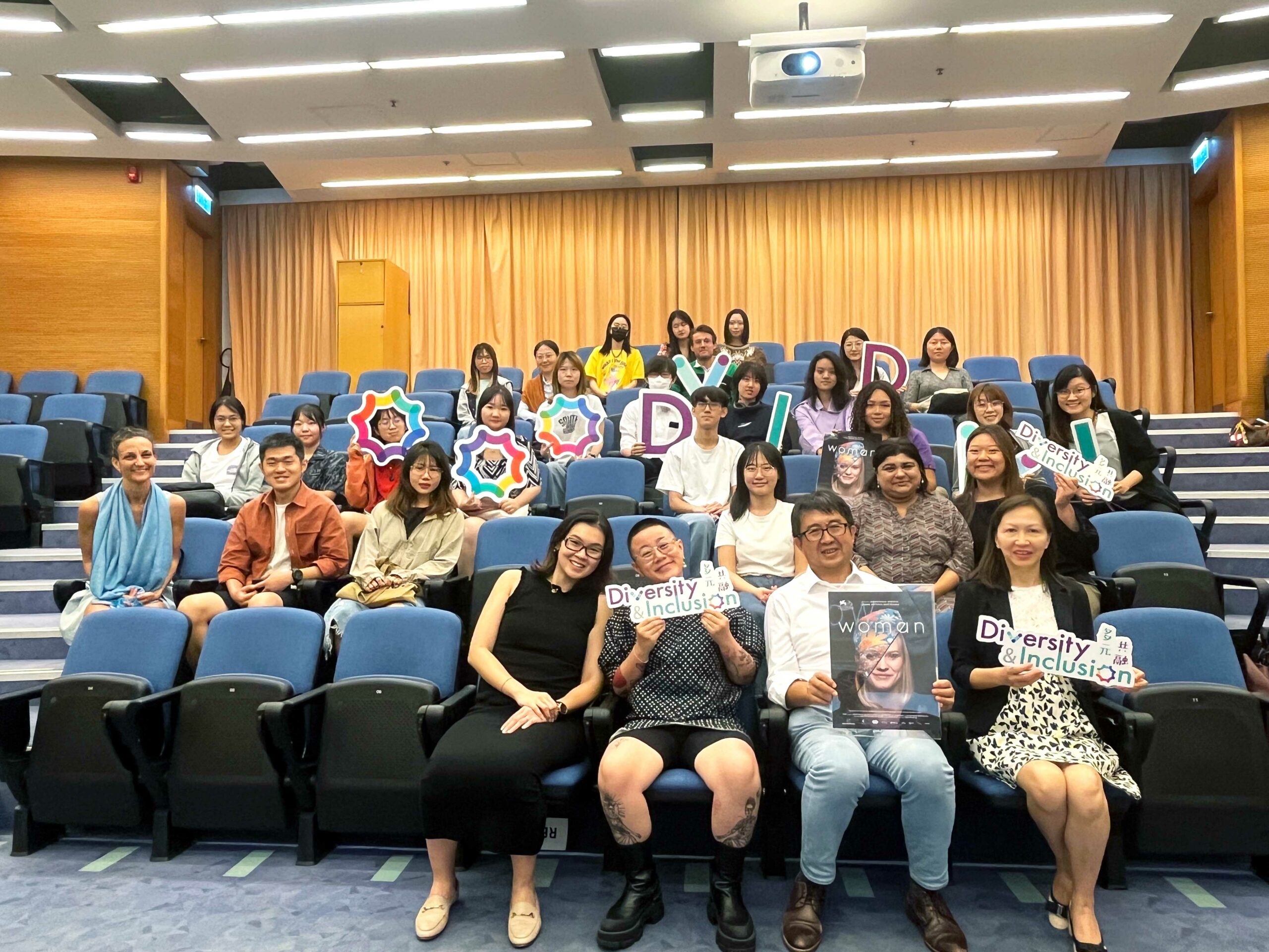 Audience members are taking a group photo at the event 'Exclusive Premiere Movie Screening of WOMAN & Post-screening Dialogue,' holding props and the movie poster.