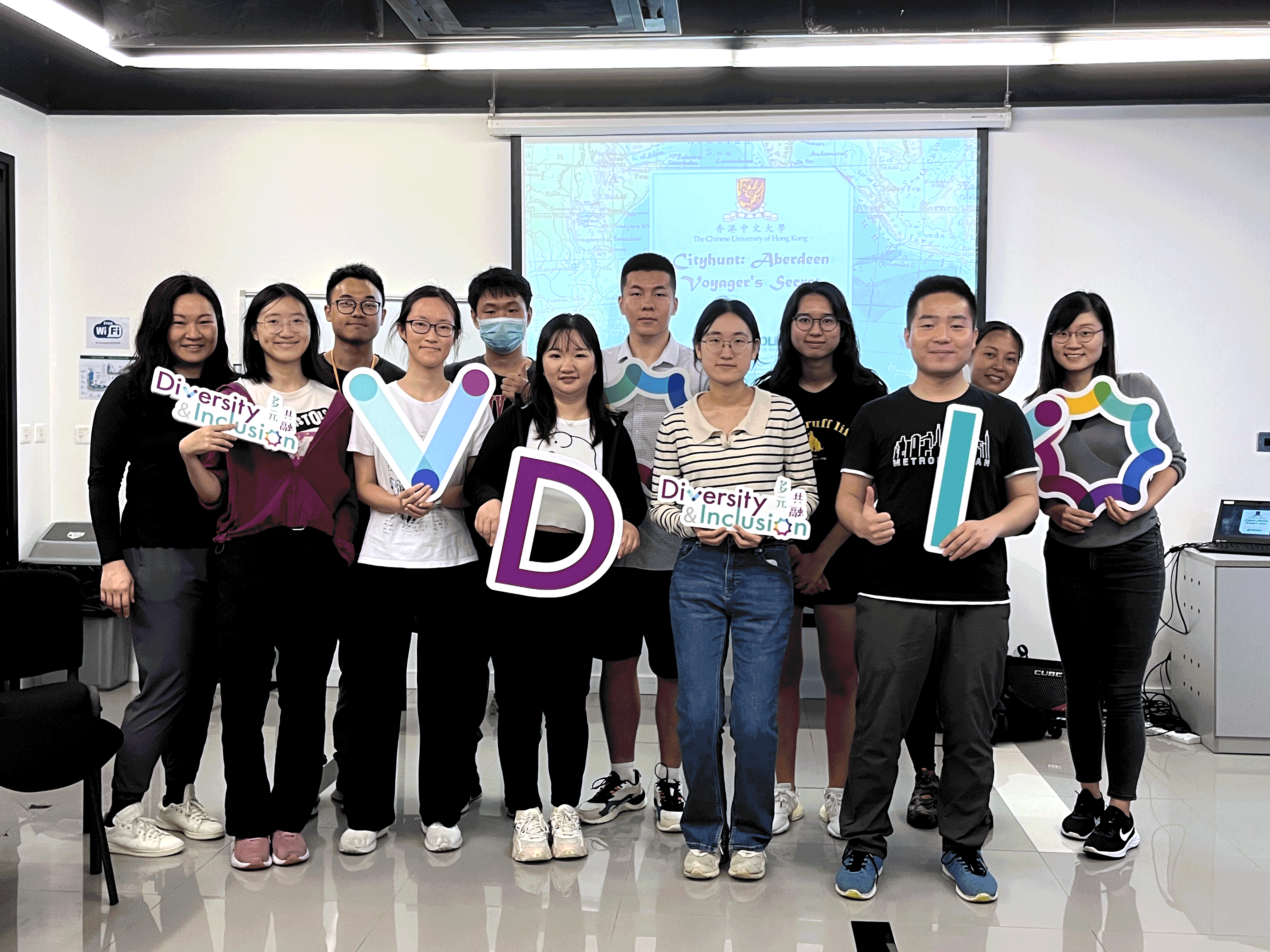 Participants of the activity stand in front of a electronic backdrop, holding the props of "DIVERSITY & INCLUSION".